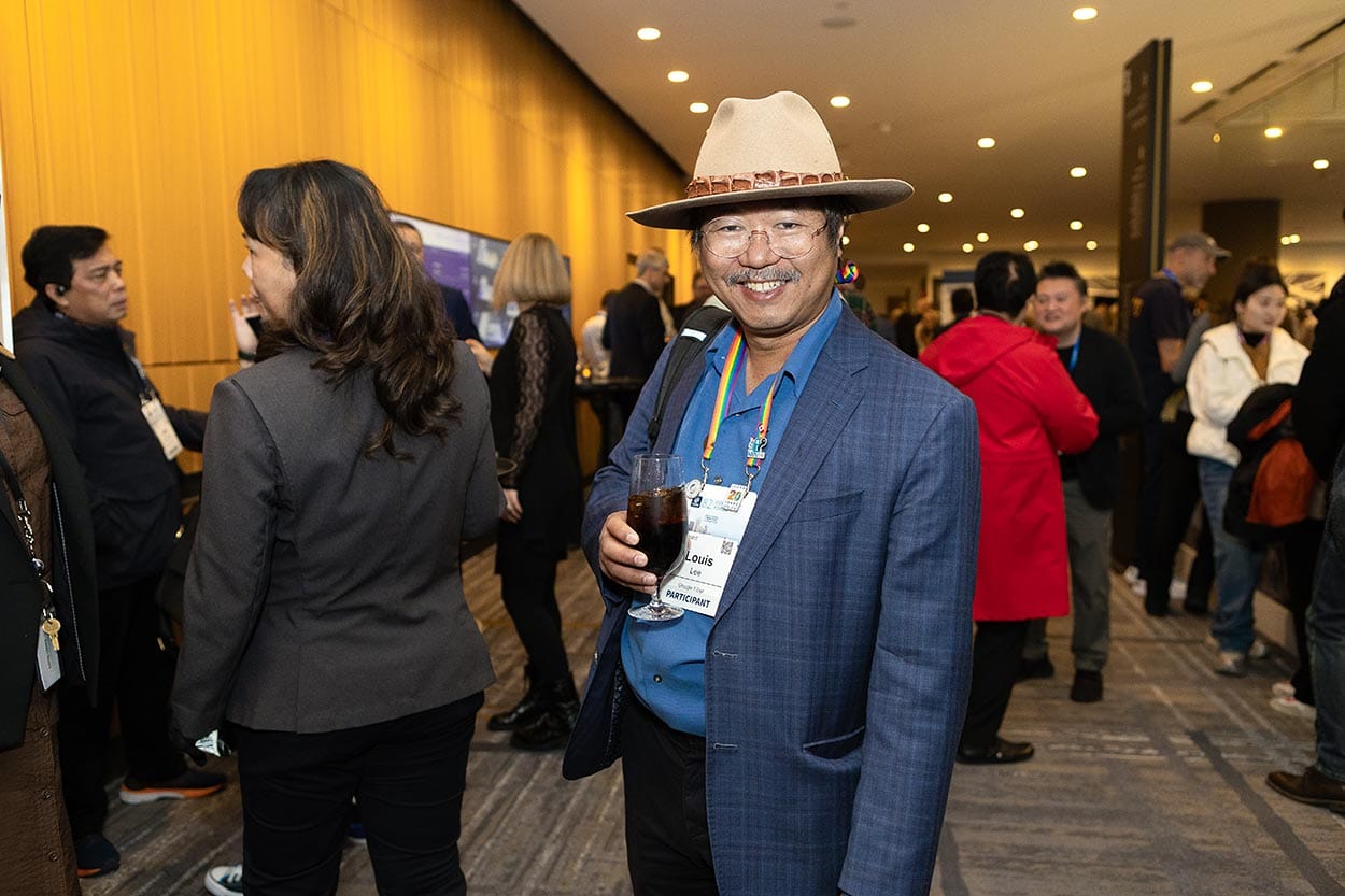 Man with a hat and event lanyard, smiling in the crowd