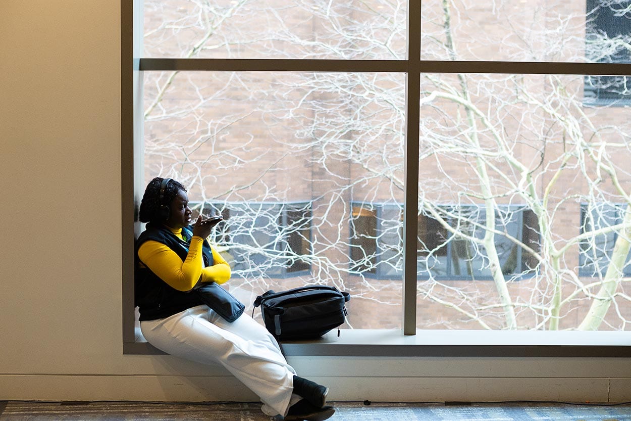 woman sitting in a window frame, on the phone with the texture of trees in the background