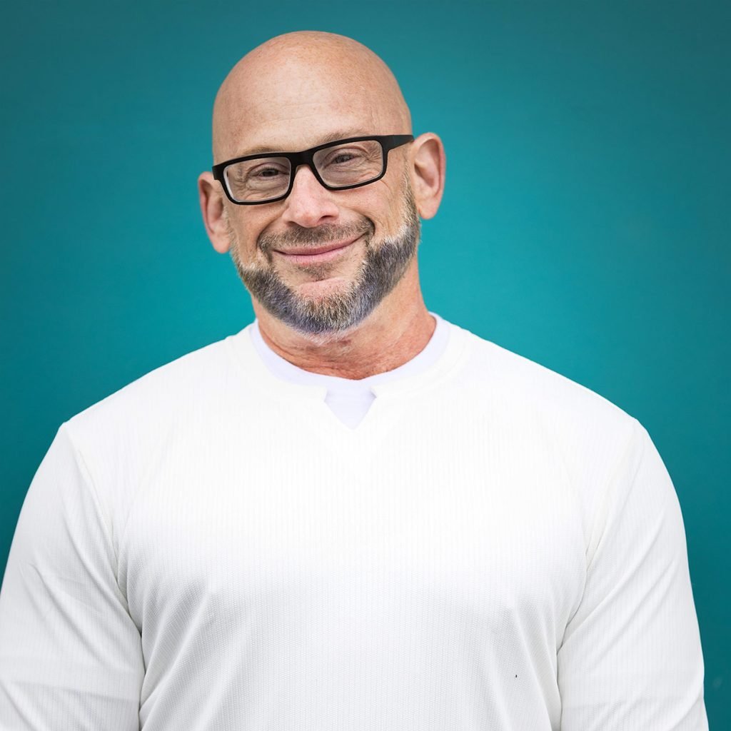 Fit man in white shirt, cool glasses standing against a bright blue door